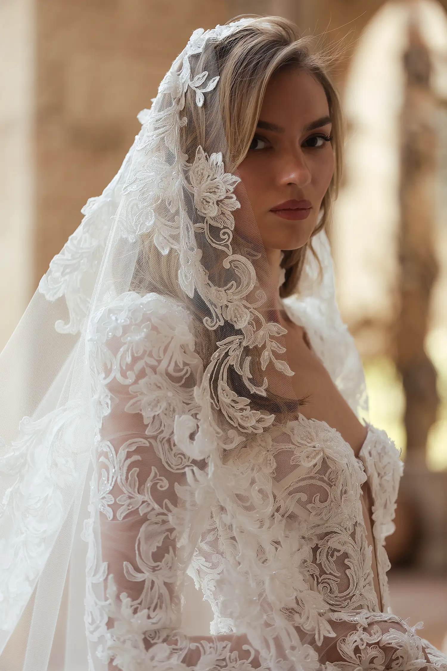 Beaded, dimensional flower embroidered boroque lace and silk organza ballgown, with tiered cutout skirt, high collar, and long puff sleeves. Shown with cathedral-length mantilla veil with beaded dimensional floral appliqué. 