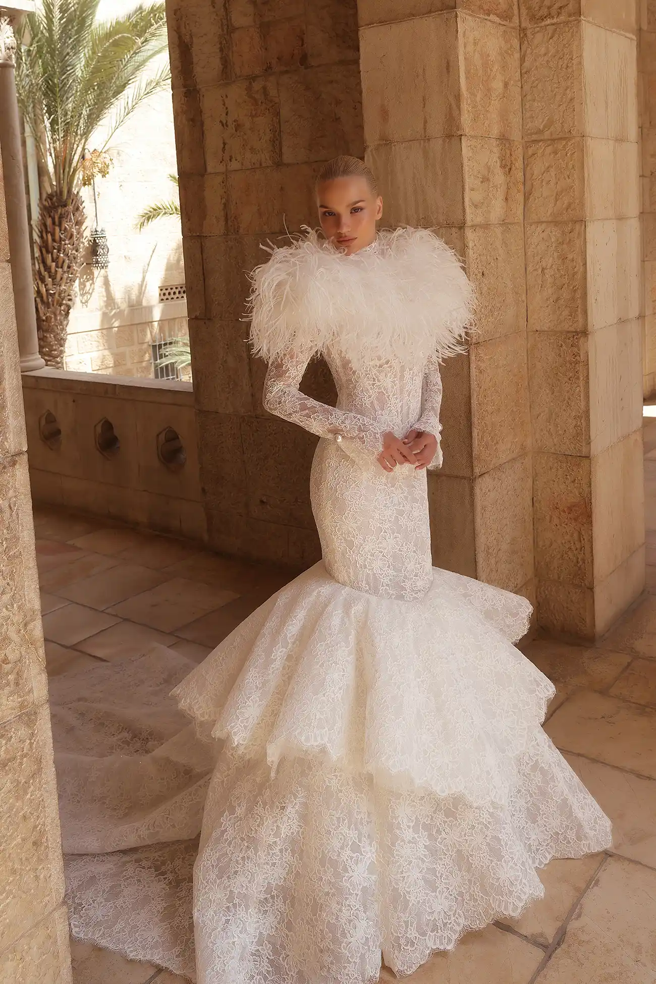 High-neck alençon lace mermaid gown with basque waist, tiered skirt, long puff sleeves, and pearl buttons.