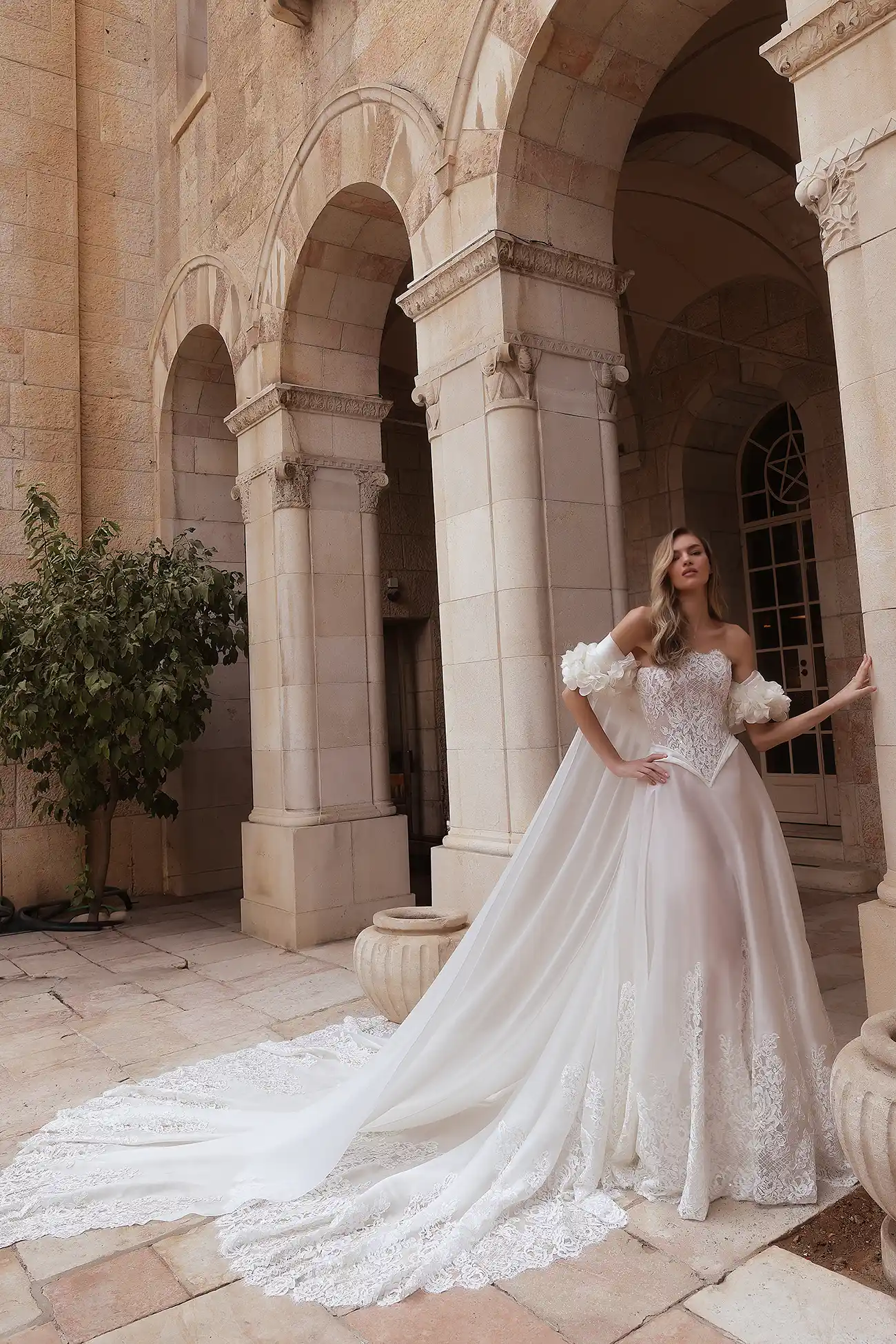 Round-neck strapless corded lace and silk organza A-line gown with lace cutout border and draped organza basque waist detail. Shown with matching silk organza cape with lace cutout train and handmade silk organza flowers.