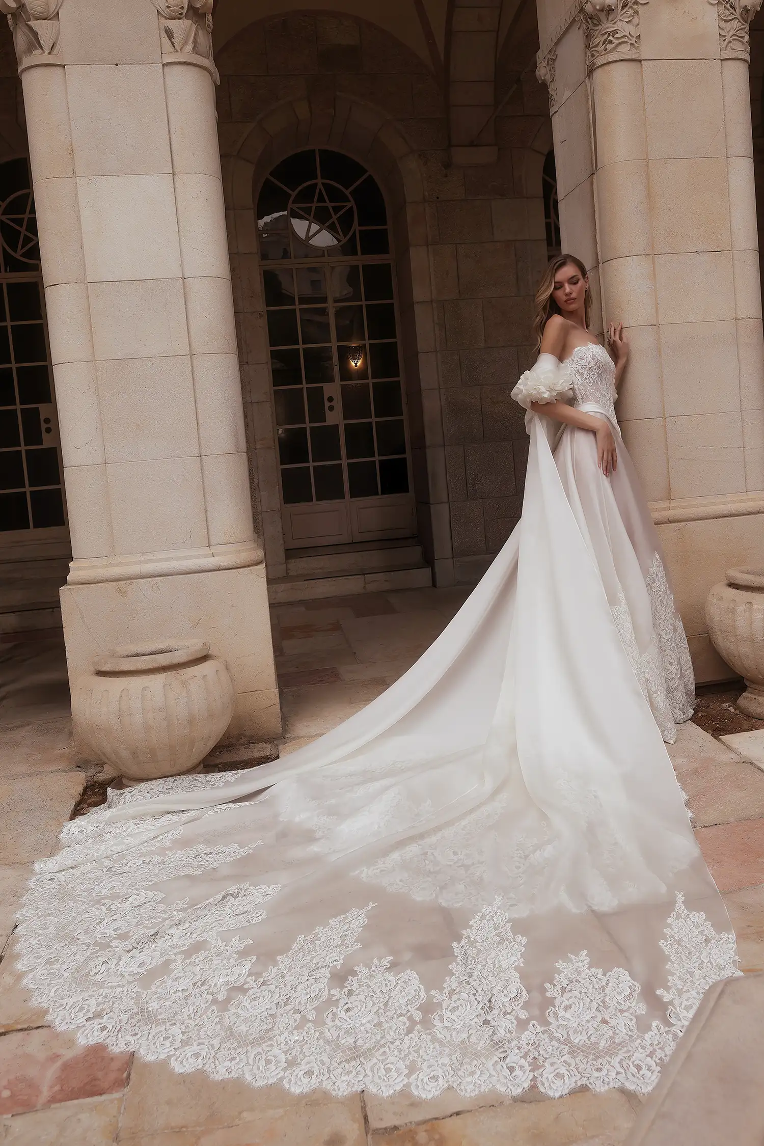 Round-neck strapless corded lace and silk organza A-line gown with lace cutout border and draped organza basque waist detail. Shown with matching silk organza cape with lace cutout train and handmade silk organza flowers.