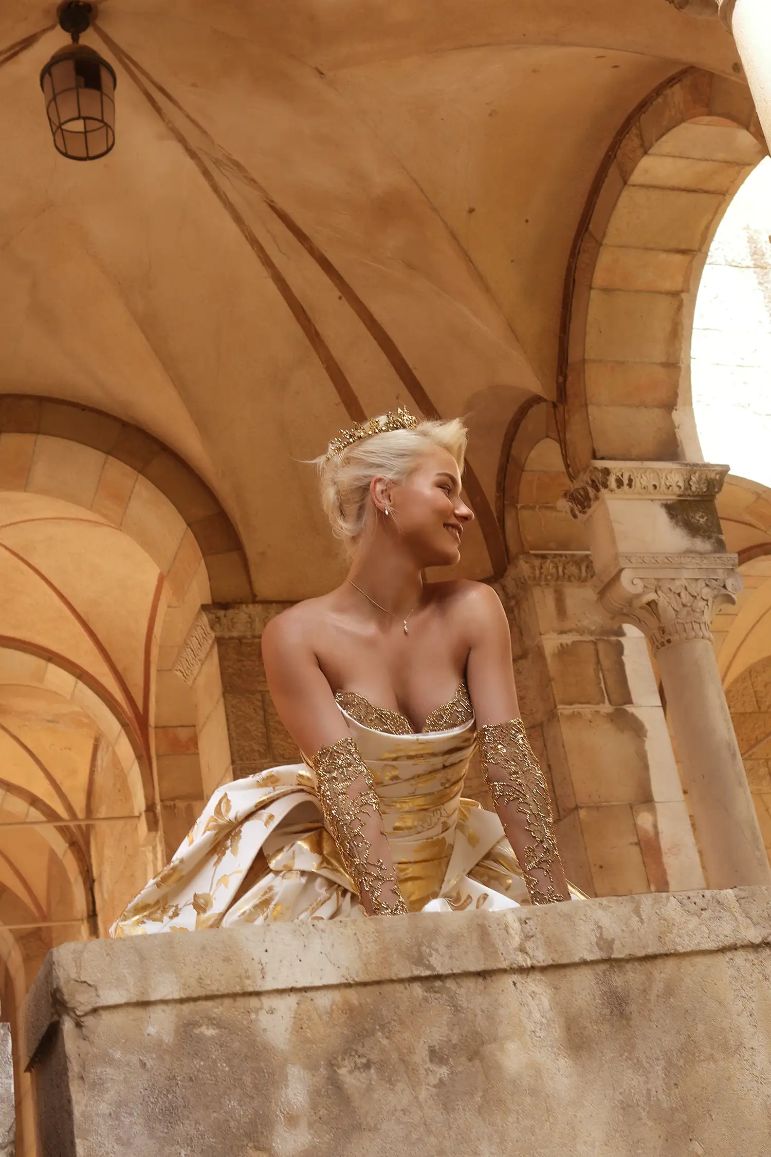 Strapless ballgown in matte satin printed with gold foil peonies, with signature Pnina bow, draped basque waist bodice and gold crystal embellished bust detail. Shown with matching gold crystal metallic chantilly lace gloves.