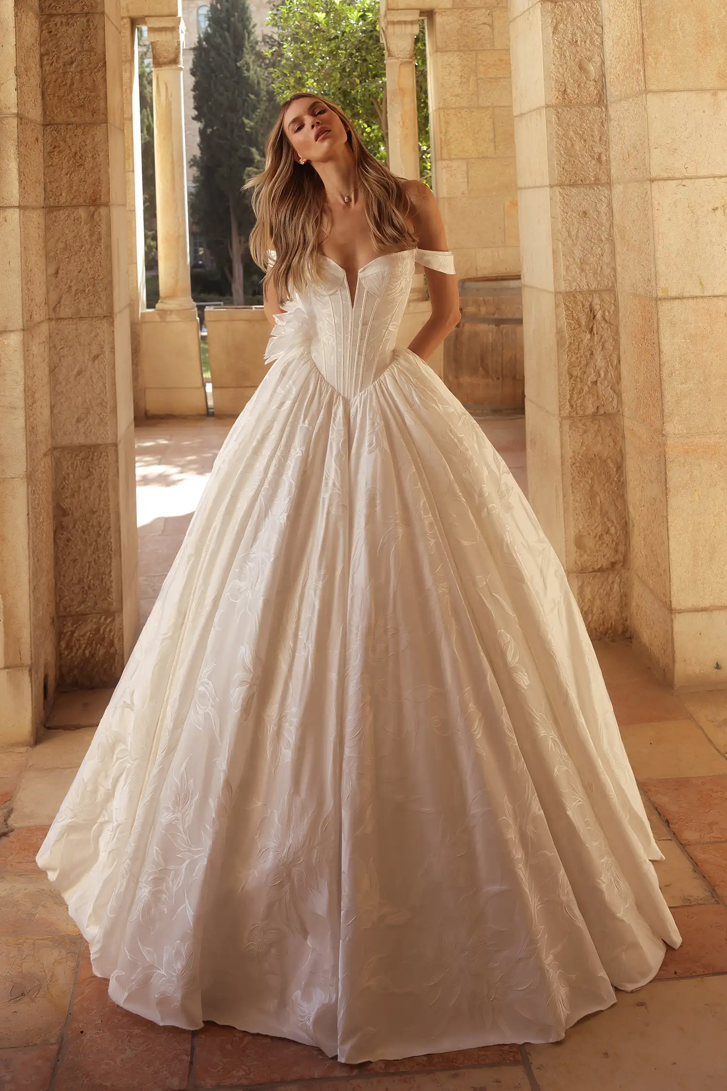 Sweetheart neckline ballgown in hand-painted silk jacquard with pointed basque waist, off-the-shoulder straps, and dimensional organza flowers. Shown with chantilly lace gloves.