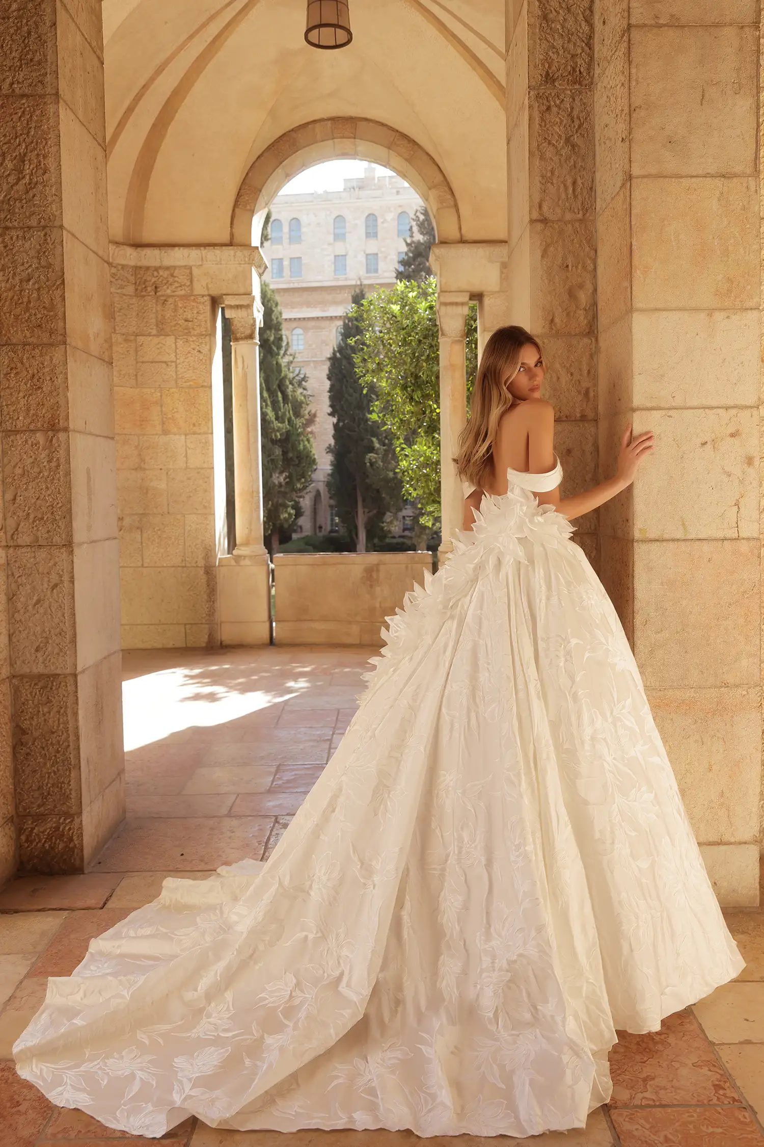 Sweetheart neckline ballgown in hand-painted silk jacquard with pointed basque waist, off-the-shoulder straps, and dimensional organza flowers. Shown with chantilly lace gloves.