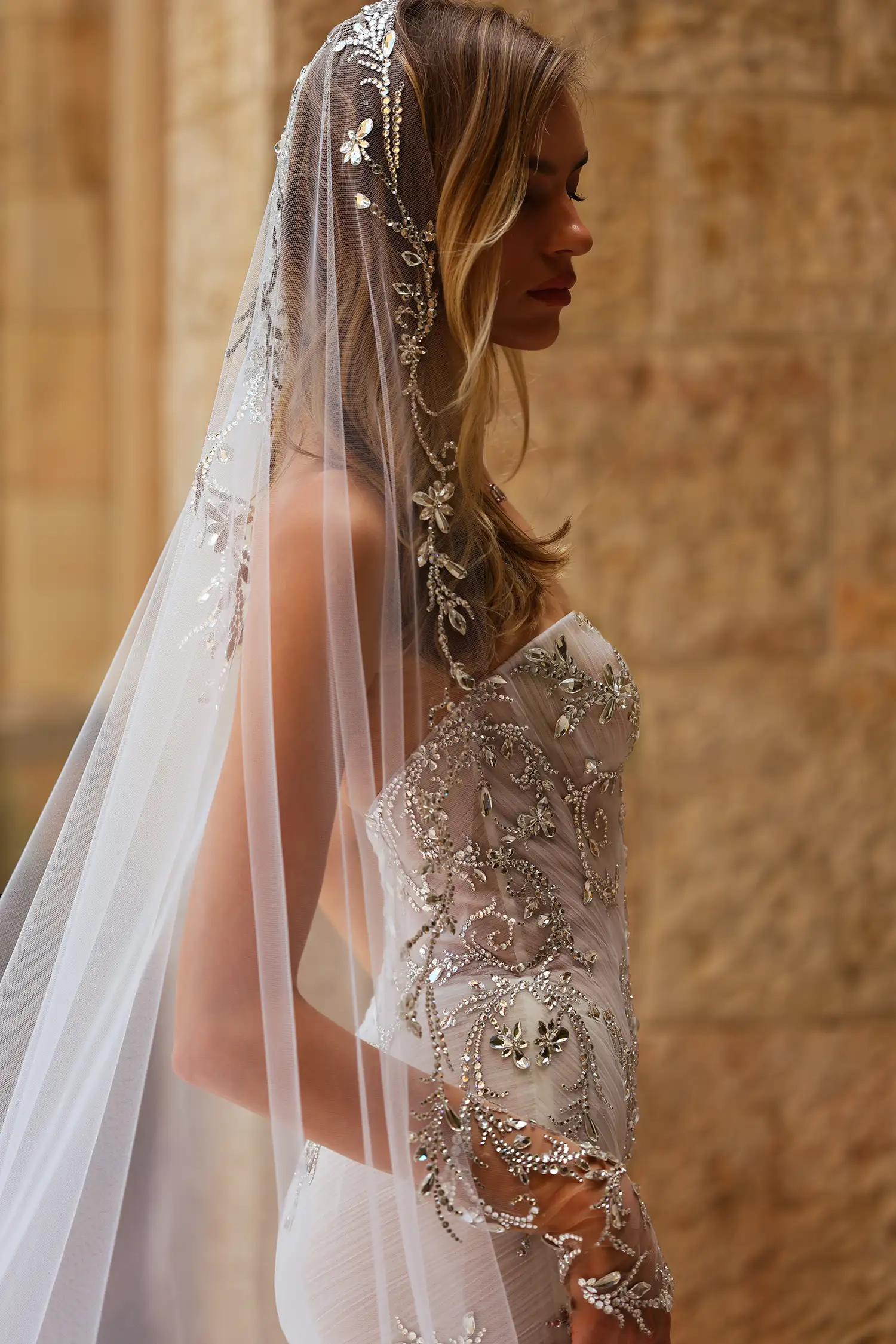 Strapless, sweetheart mermaid gown in tulle plissé fully embellished in mirror crystals. Shown with mirror crystal appliqué illusion gauntlet gloves and cathedral-length mirror crystal mantilla veil.