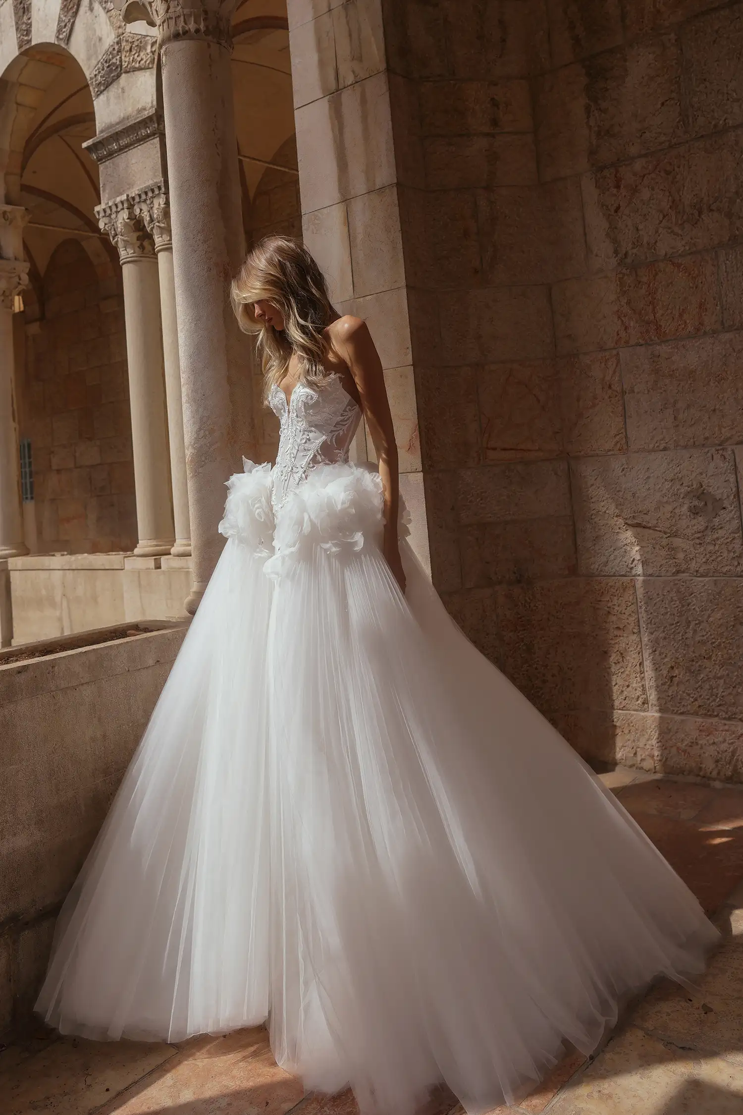 Strapless ballgown in satin and sunray pleated tulle, with cat-eye sweetheart neckline, water crystal appliqués and water crystal drops, and dimensional organza flowers at hips.