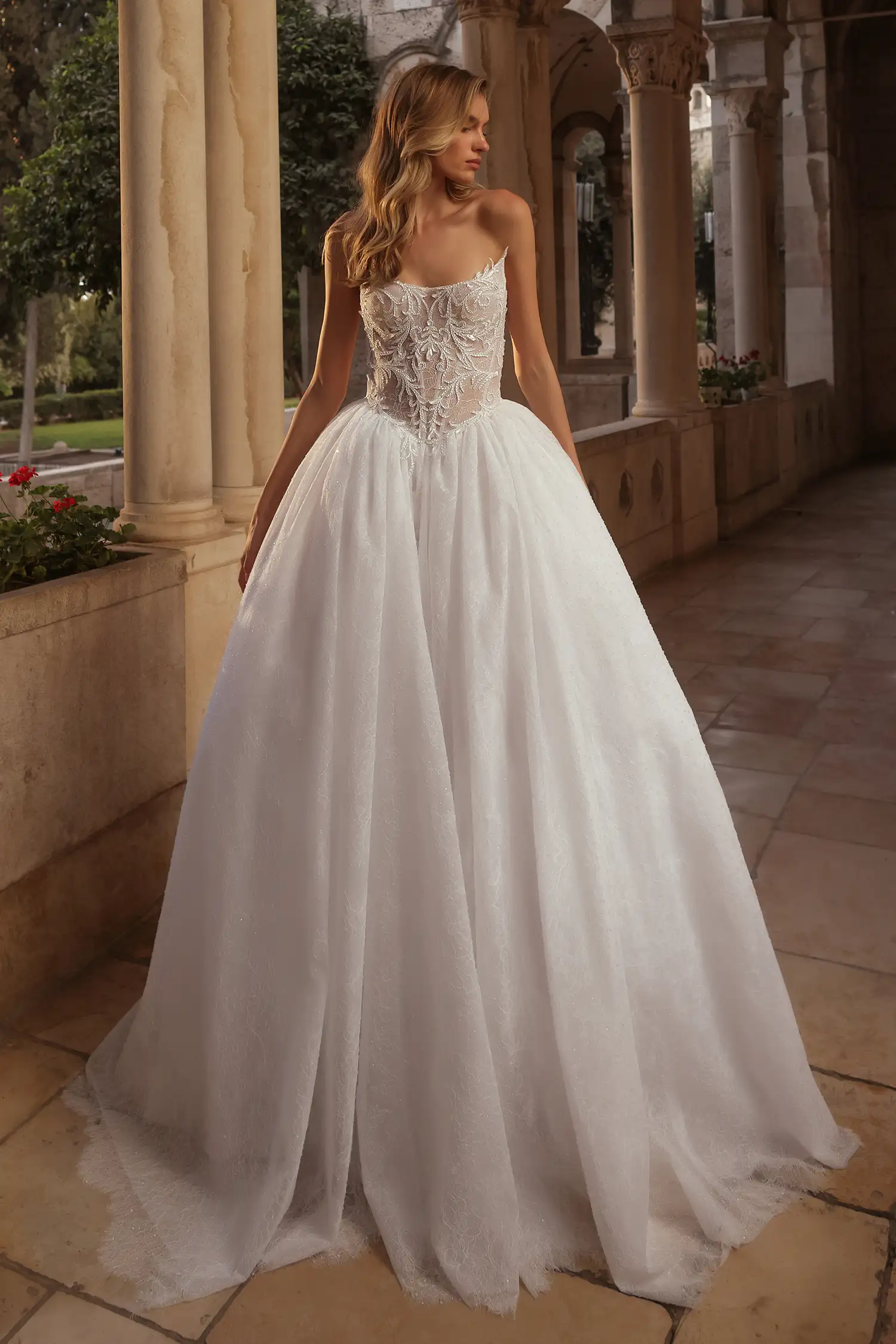 Strapless ballgown fully beaded with water crystals, with sheer bodice, water crystal appliqué, and chantilly lace handmade dimensional flowers at back waistline. Shown with chantilly lace and water crystal gauntlet gloves.