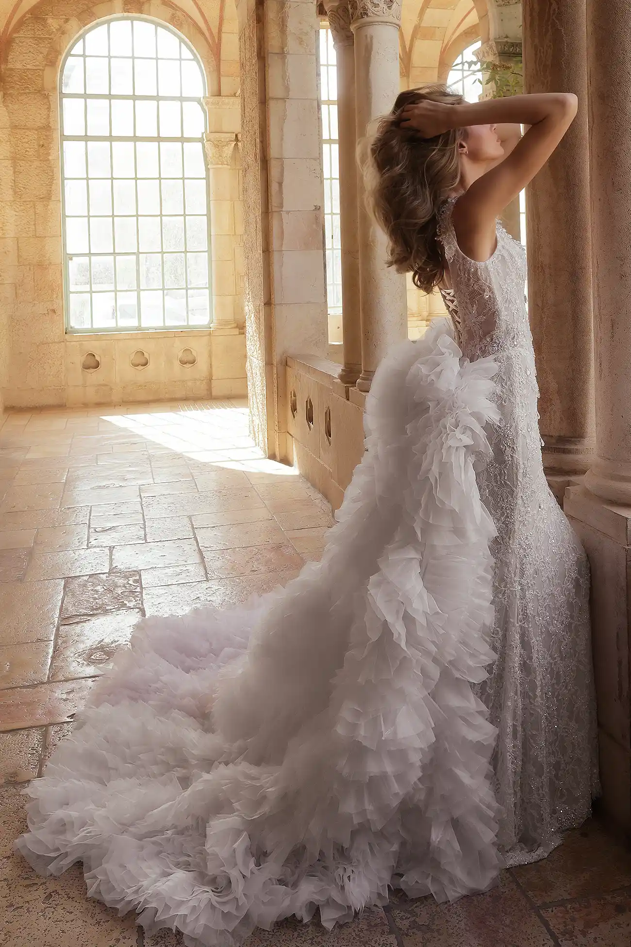 Hand-beaded chantilly lace sheath gown with portrait neckline embellished with water crystal droplets. Shown with detachable train in handmade organza flowers.