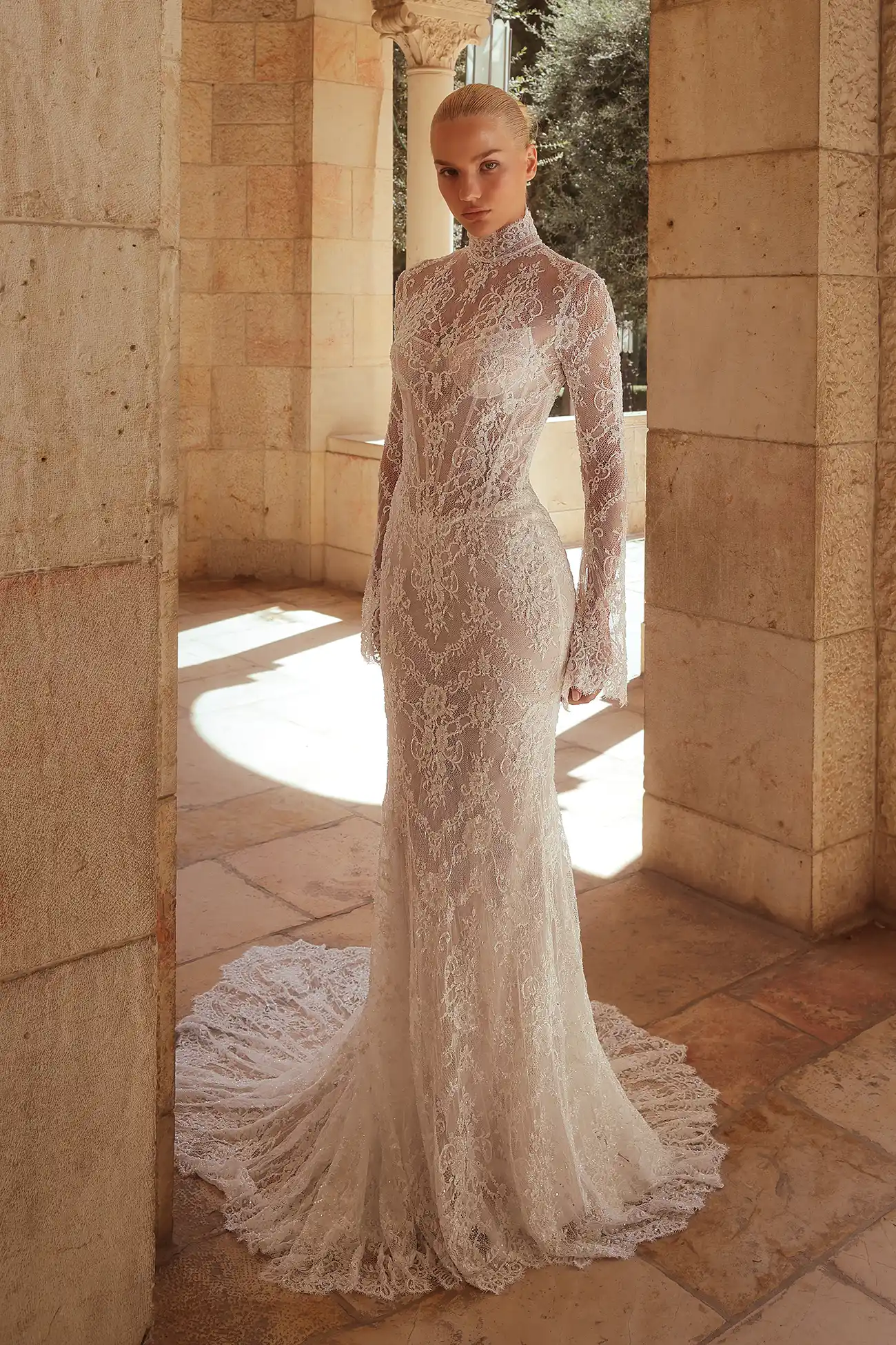 Hand-beaded chantilly lace sheath gown with high neckline, long bell sleeves, and sheer open back with water crystal tassels.