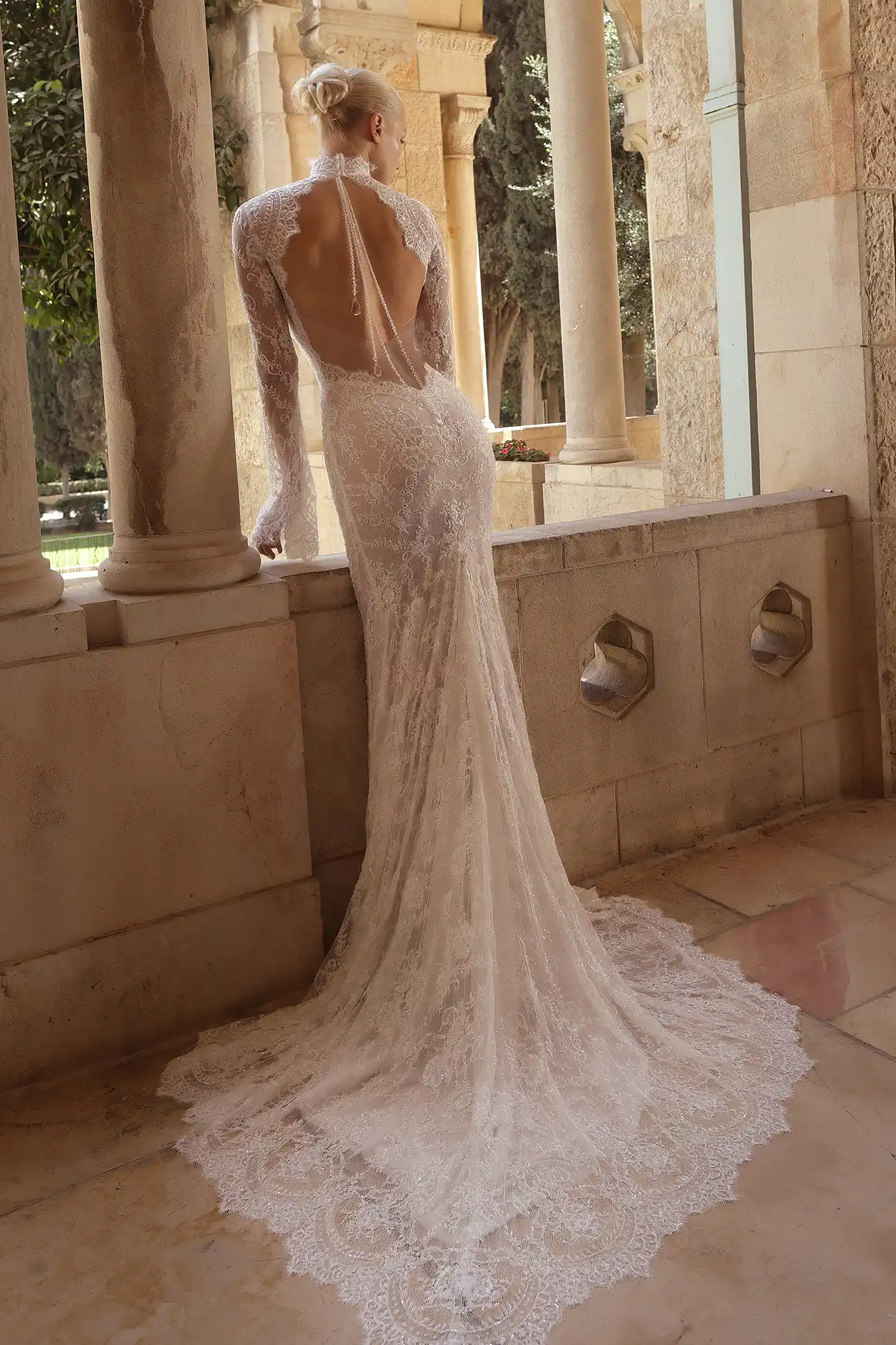 Hand-beaded chantilly lace sheath gown with high neckline, long bell sleeves, and sheer open back with water crystal tassels.