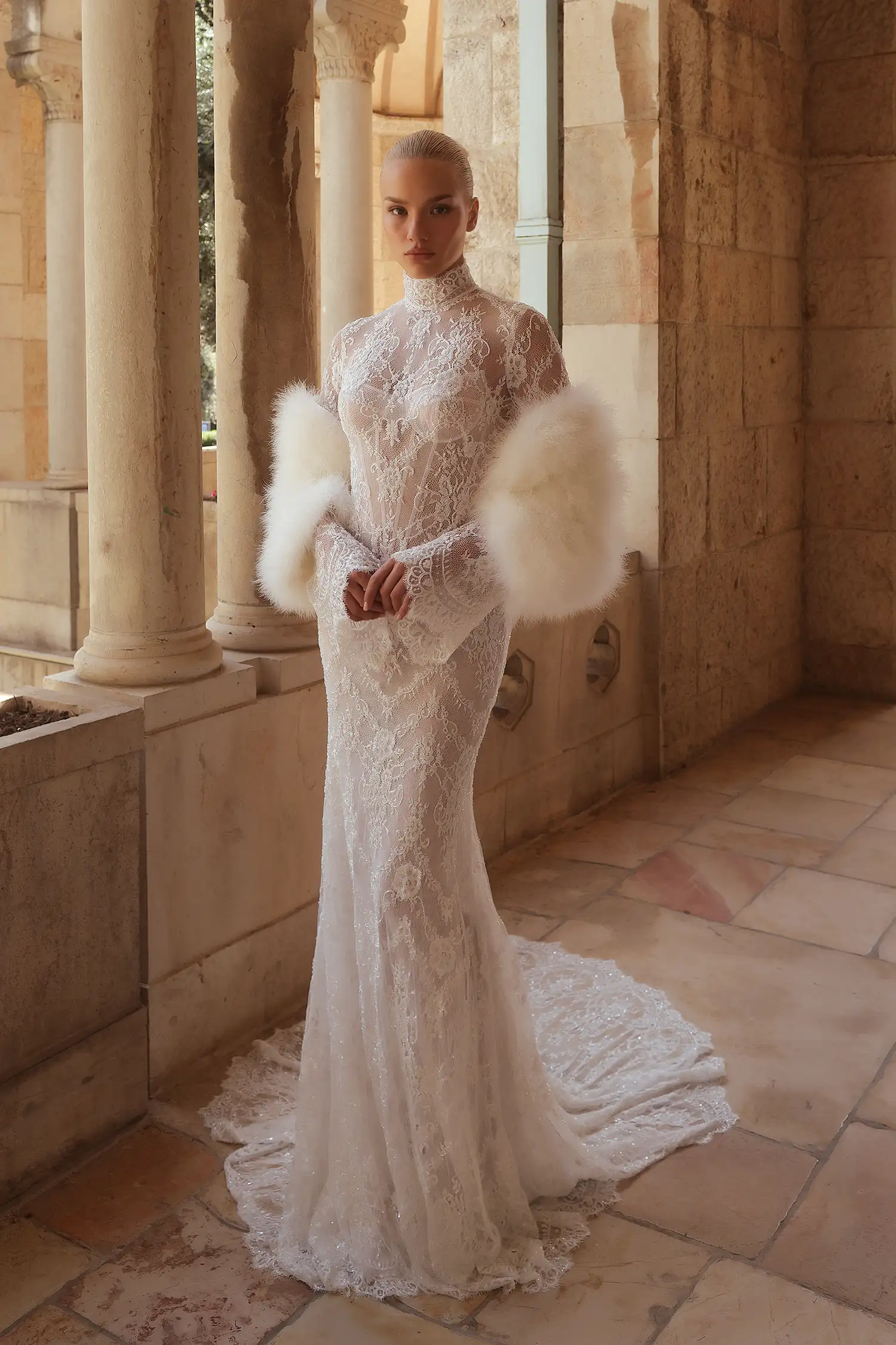 Hand-beaded chantilly lace sheath gown with high neckline, long bell sleeves, and sheer open back with water crystal tassels.